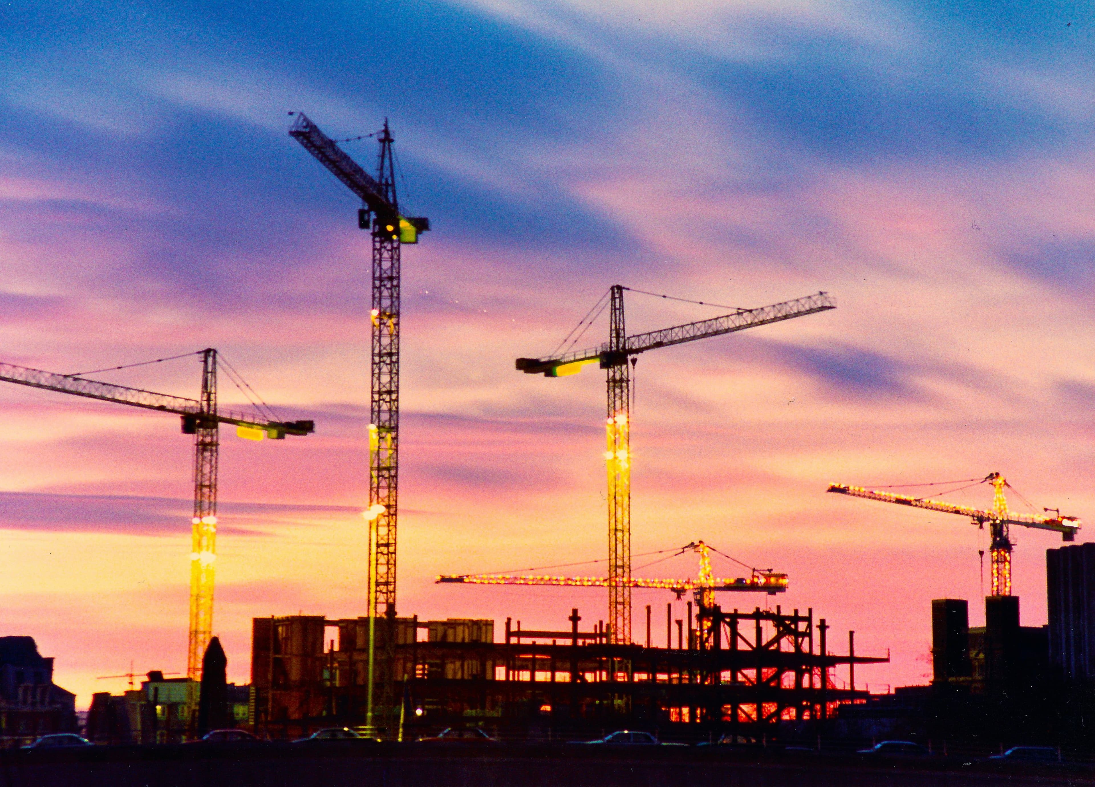 Tower cranes and the steel frame of a construction site at dusk